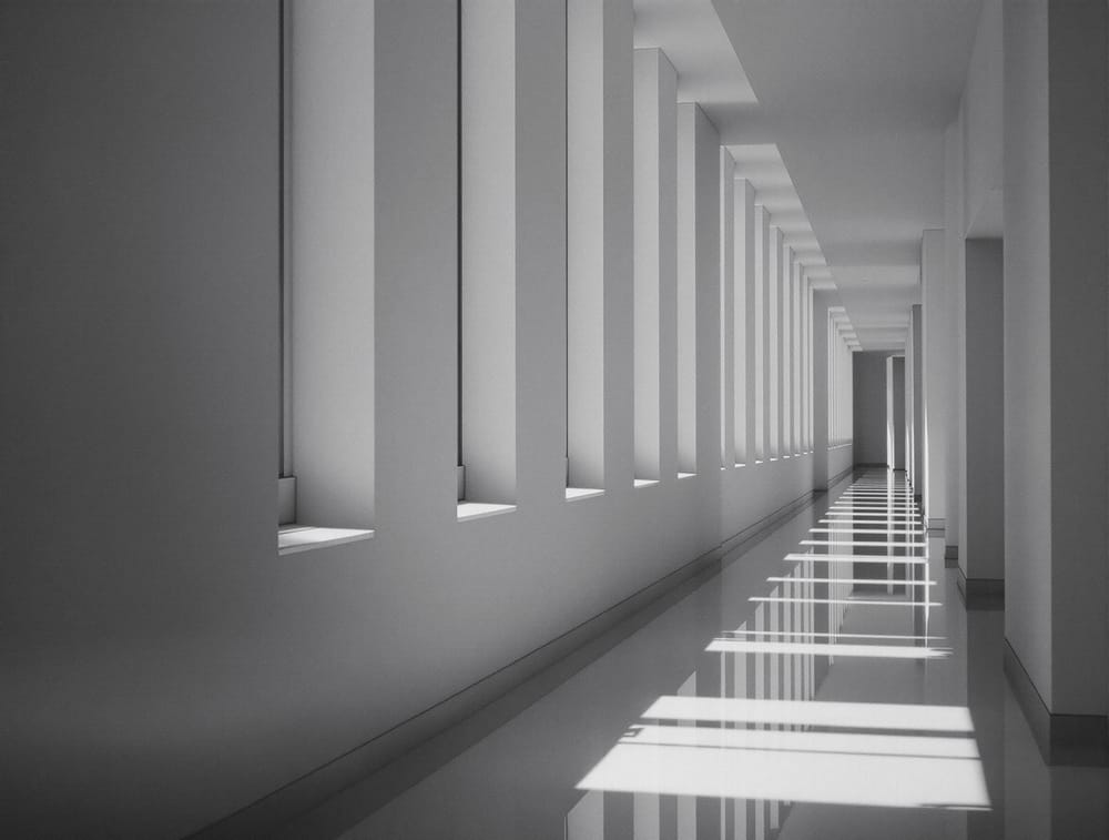 A calm empty architectural corridor with strong natural light from tall side windows and no signage.